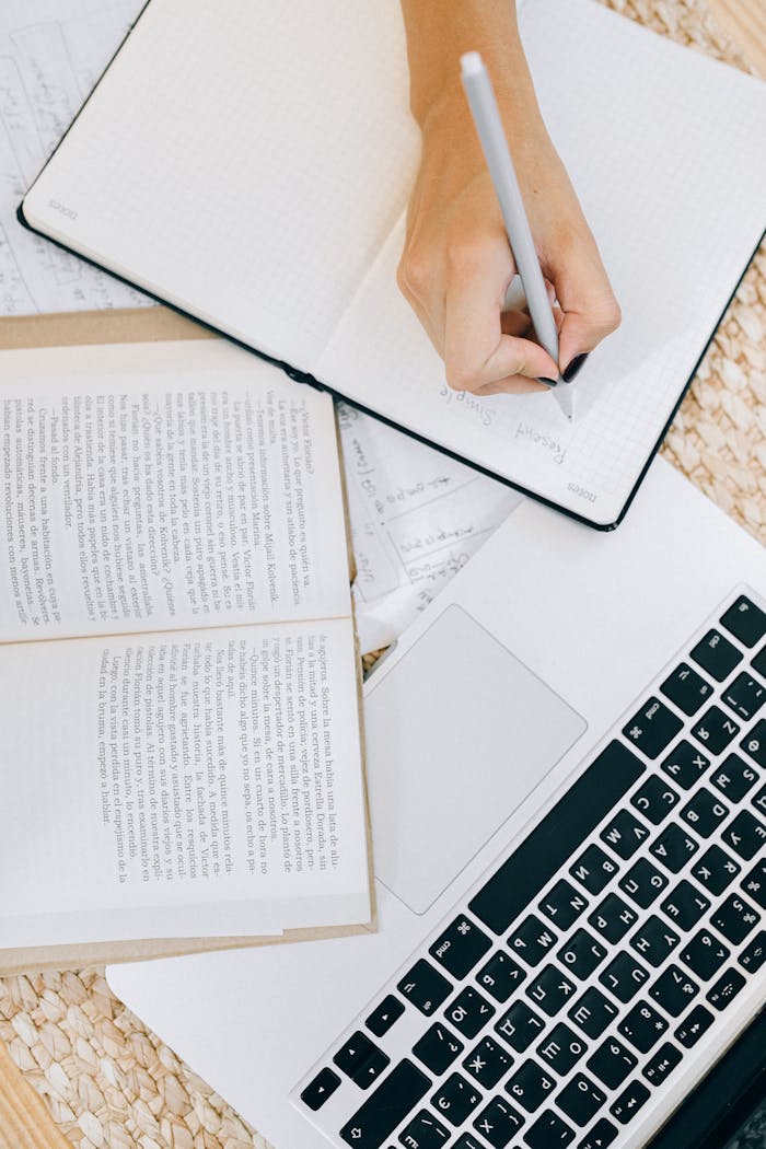 The Art of Drawing Readers In: Your attractive post title goes here Close-up of a woman's hand writing in an open notebook on a desk with a laptop and books.